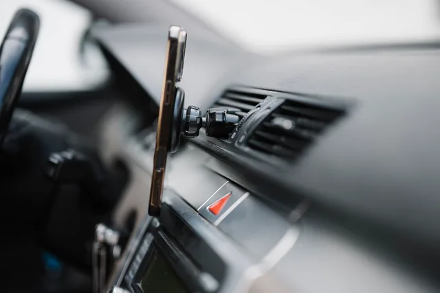 Smartphone is securely attached to the dashboard of a car. The device shows navigation apps while the driver prepares for a trip. The interior has modern design elements. Roadside navigation apps itinerary: a field-test template