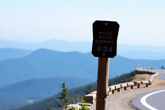 Blue Ridge Parkway milepost sign beside a mountain overlook on the ridgeline. Blue Ridge Parkway signs compared with US Route 66 markers