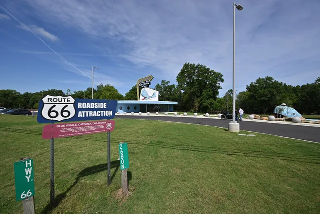 The Route 66 Roadside Attraction sign, with the brand-new Blue Whale of Catoosa visitor center behind it, and the Blue Whale to the right. 2600 OK-66, Catoosa, Oklahoma 74015. Roadside attractions booking: what to ask before you pay