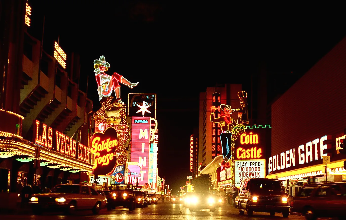 Fremont Street — at night in Downtown Las Vegas in 1983. With vintage neon signs, including "Vegas Vickie" on the left, and " Vegas Vic " cowboy on the right. Choose the bypassed town over the highway exit for a vintage sign trip